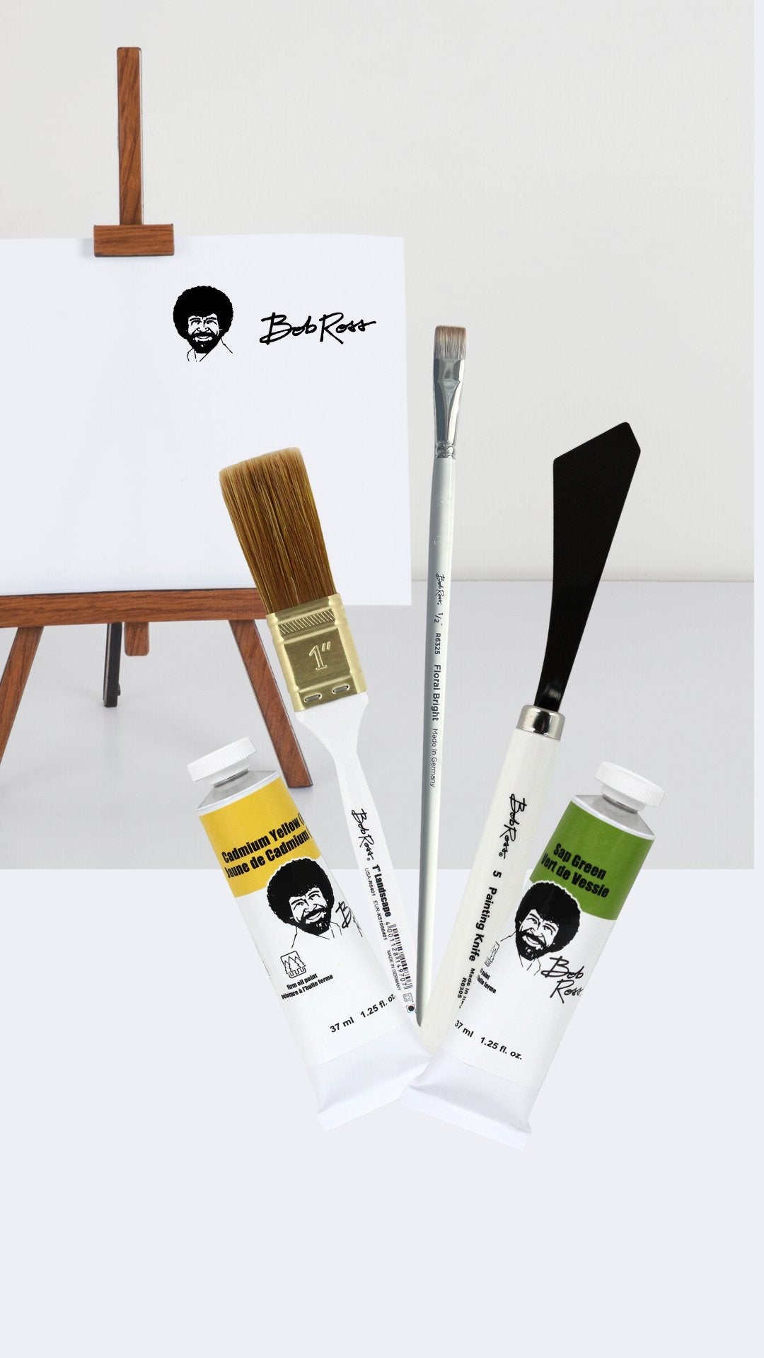 A display of Bob Ross products including 2 landscape oil paint tubes, and a selection of Bob Ross paintbrushes and a painting knife
